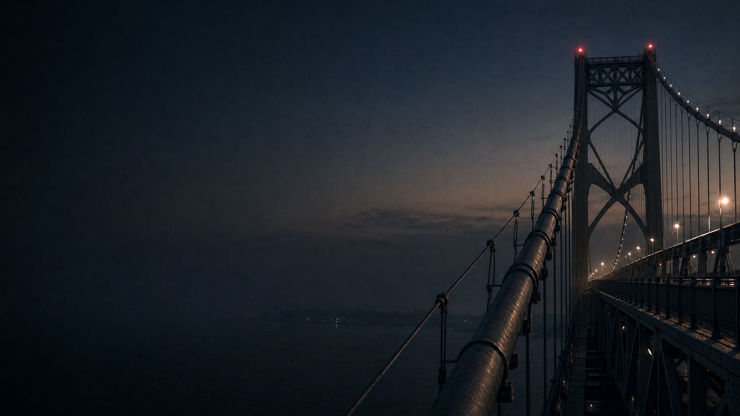 A suspension bridge at dusk with red warning lights